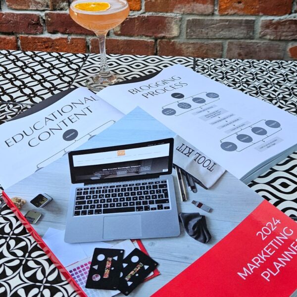 A laptop and a drink on The Marketing Planner - 2024 Edition's table.
