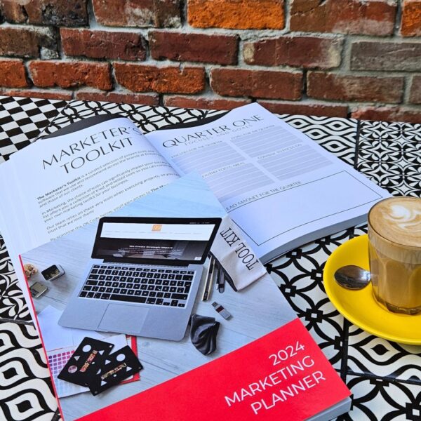 A coffee and a book on a table next to The Marketing Planner - 2024 Edition.
