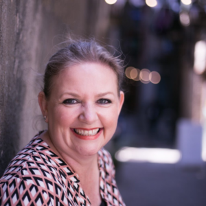 A smiling woman leaning against a wall.
