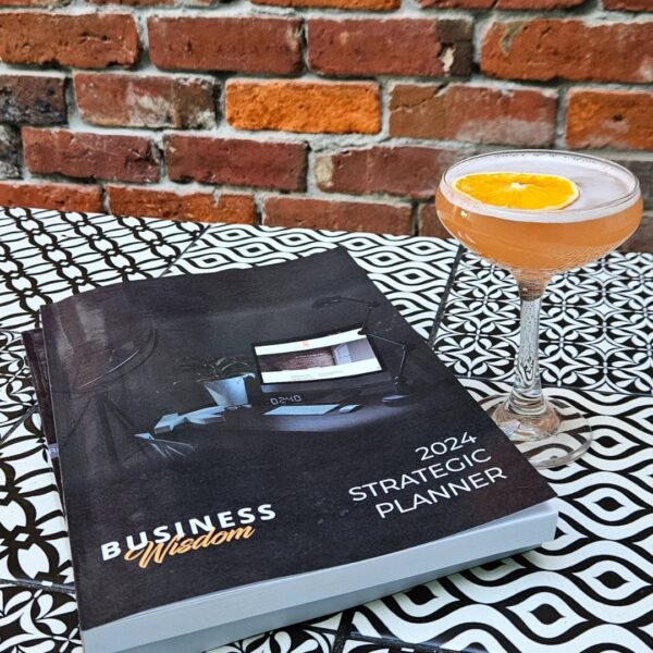 The Strategic Planner - 2024 Edition cocktail and book on a table next to a brick wall.