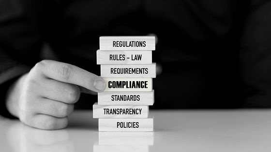 A man holding a stack of blocks with the words compliance, rules and regulations.